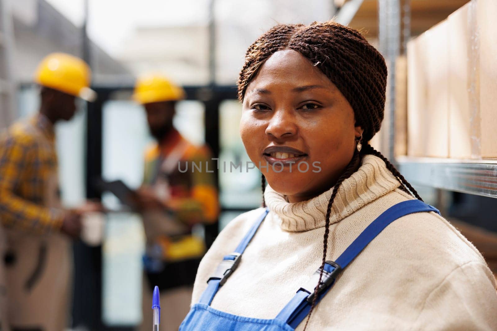Smiling african american woman working in industrial warehouse portrait. Shipment manager with positive facial expression standing near parcels shelf and looking at camera close up