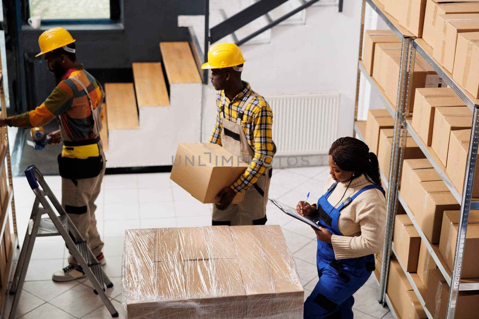 Package handlers picking order and packing parcels in warehouse. All black retail storehouse employees team inspecting packages before transportation using checklist on clipboard top view