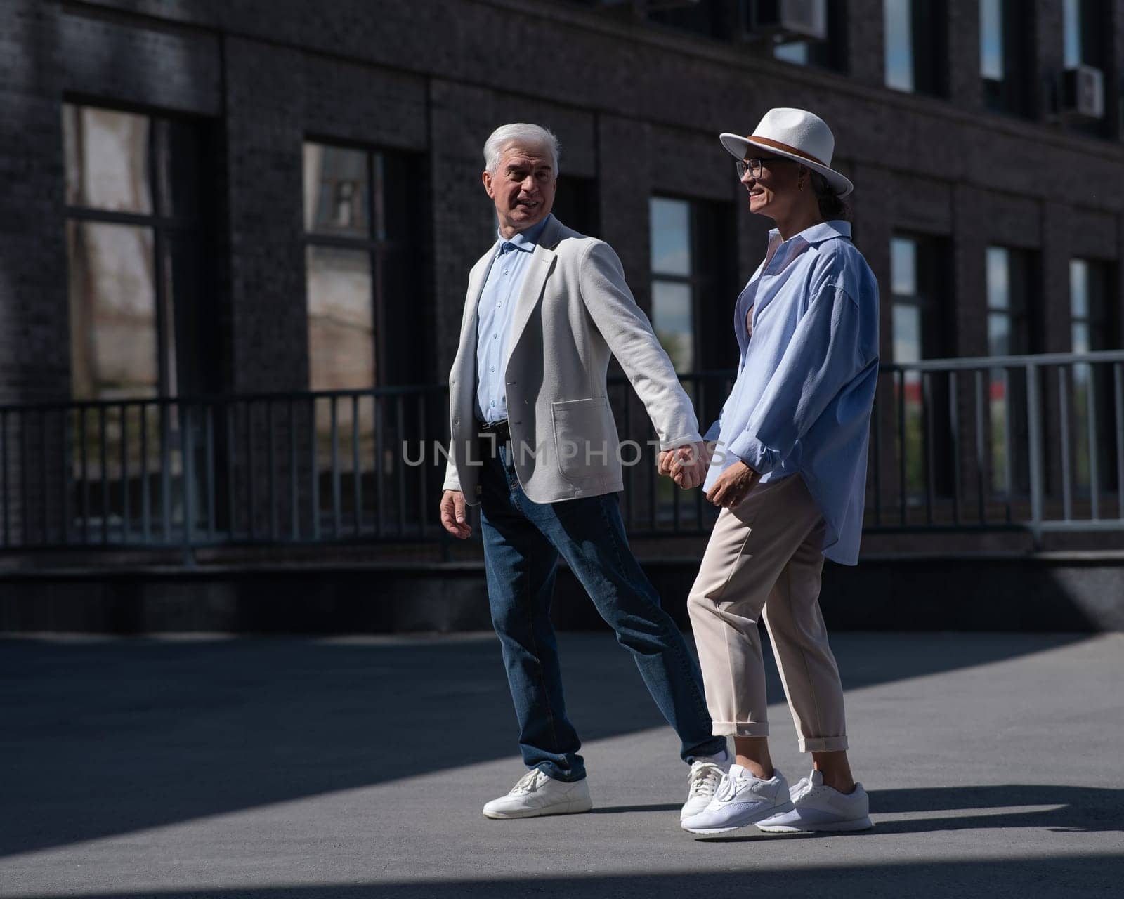 Stylish mature couple. Gray-haired man and woman holding hands while walking around the city. by mrwed54