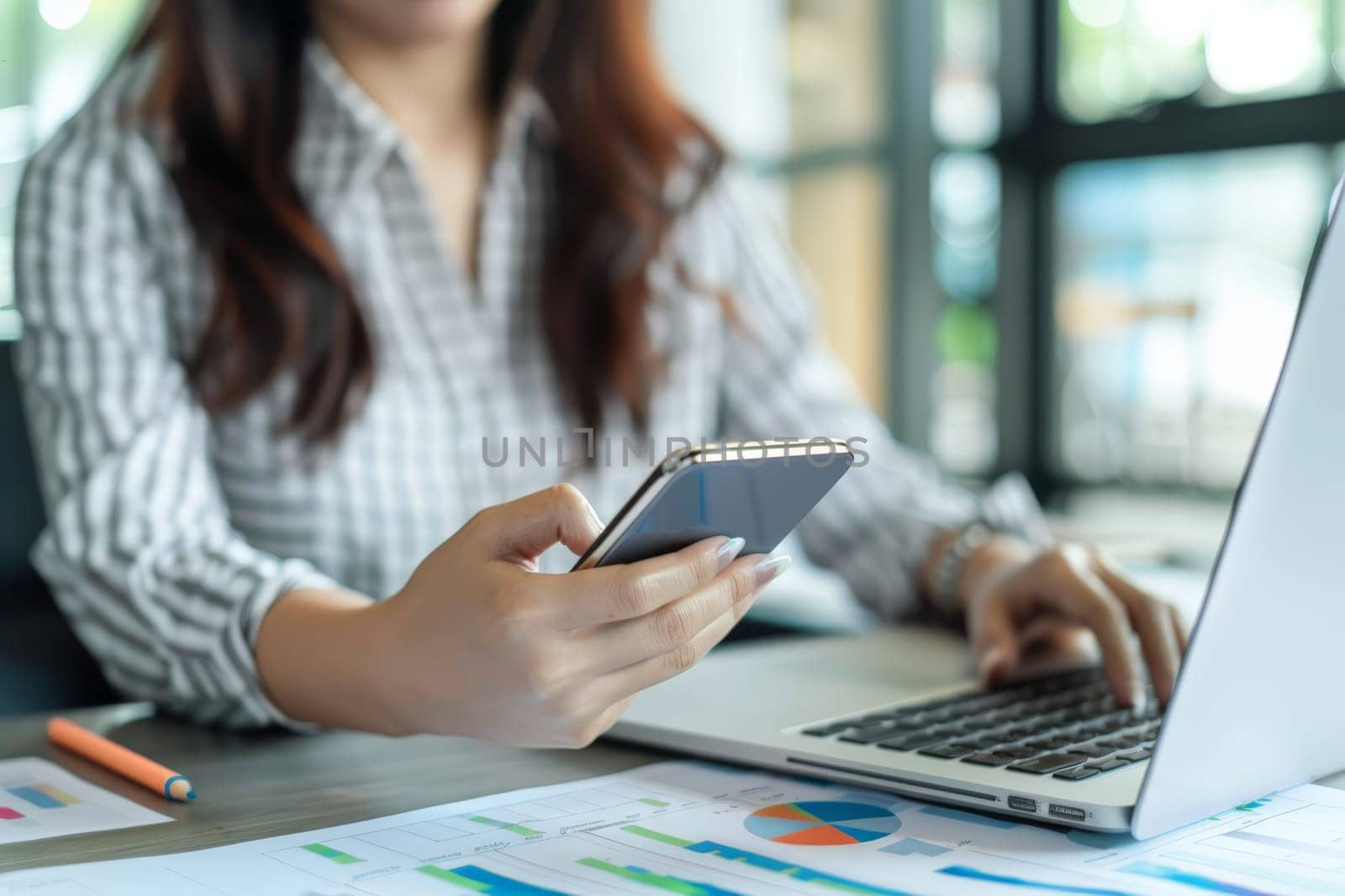 Close up of Businesswoman using smartphone while working on laptop.