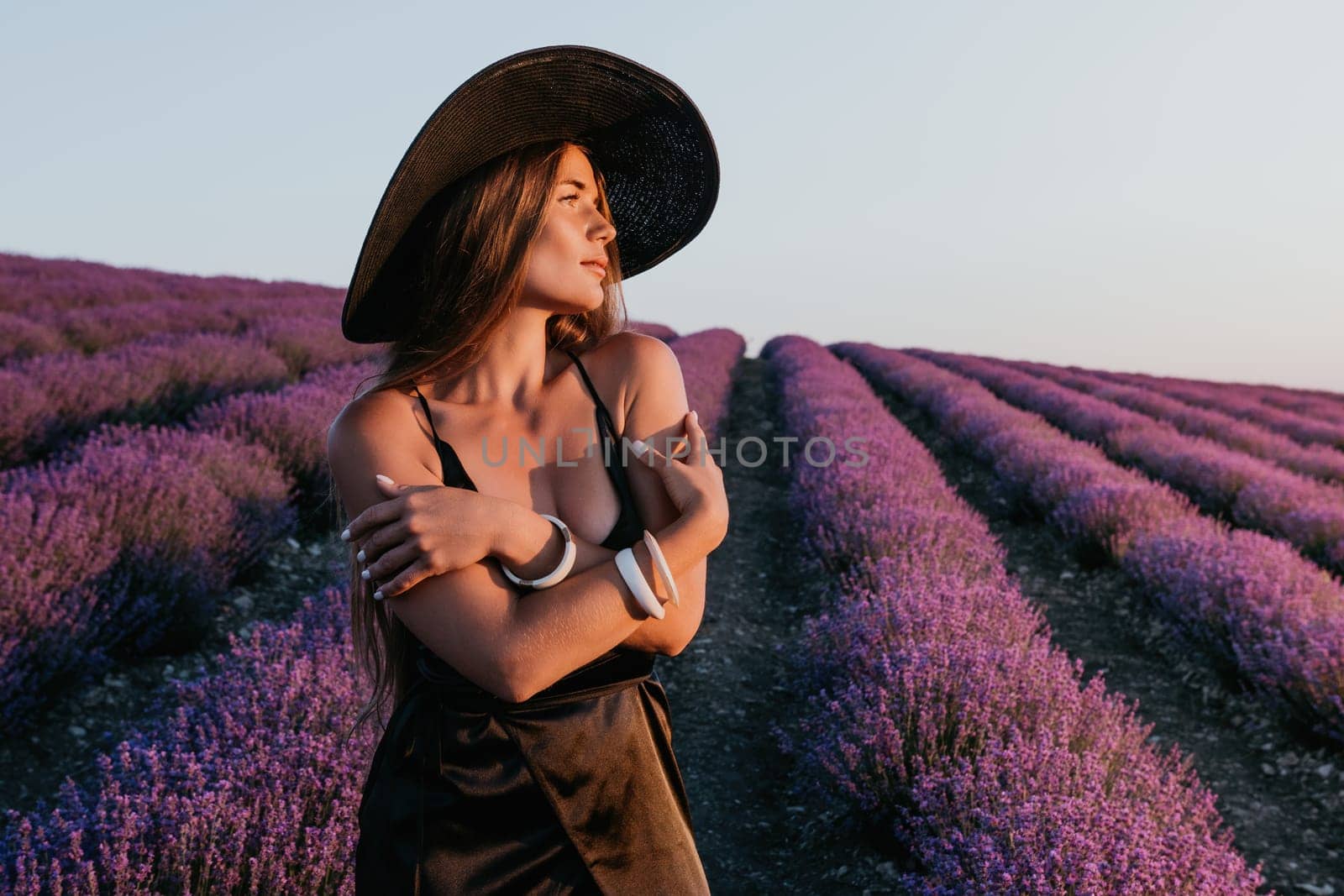 Woman lavender field. Happy carefree woman in black dress and hat with large brim walking in a lavender field during sunset. Perfect for inspirational and warm concepts in travel and wanderlust. by panophotograph