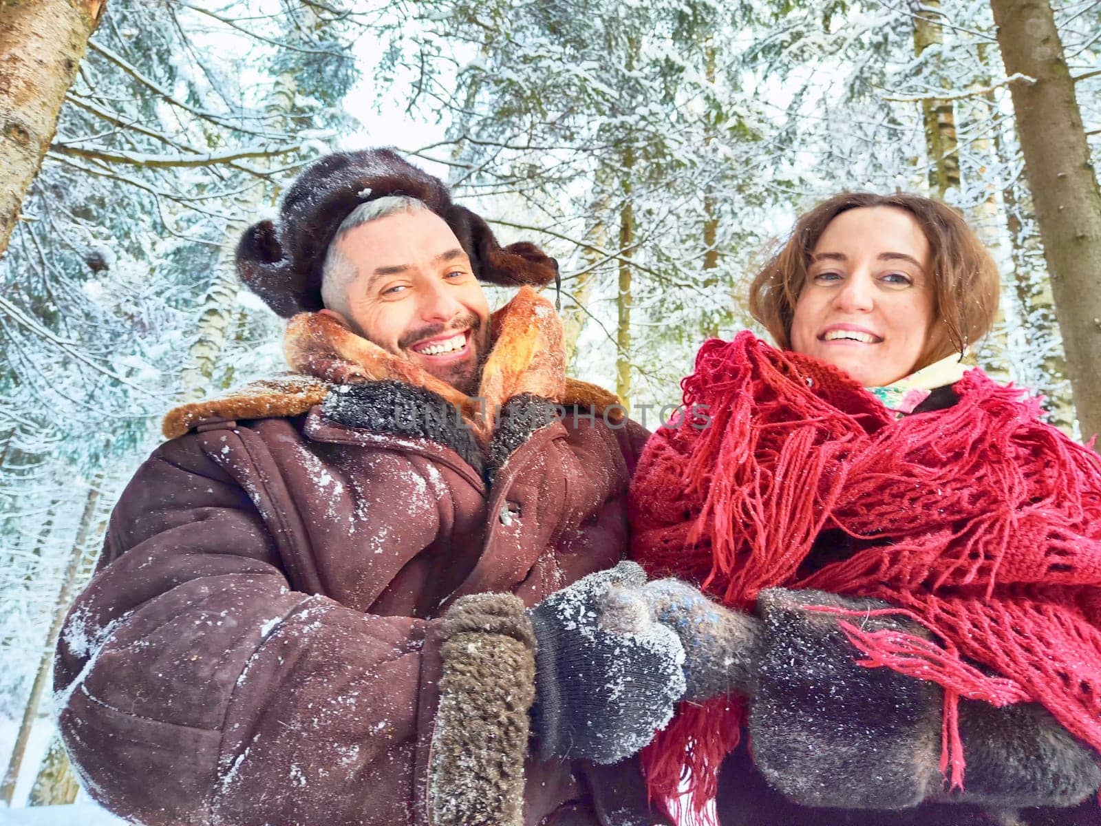 Cute middle-aged couple hugging in a snowy forest in winter. Photo shoot in stylized clothes of the USSR. Hat with earflaps, felt boots