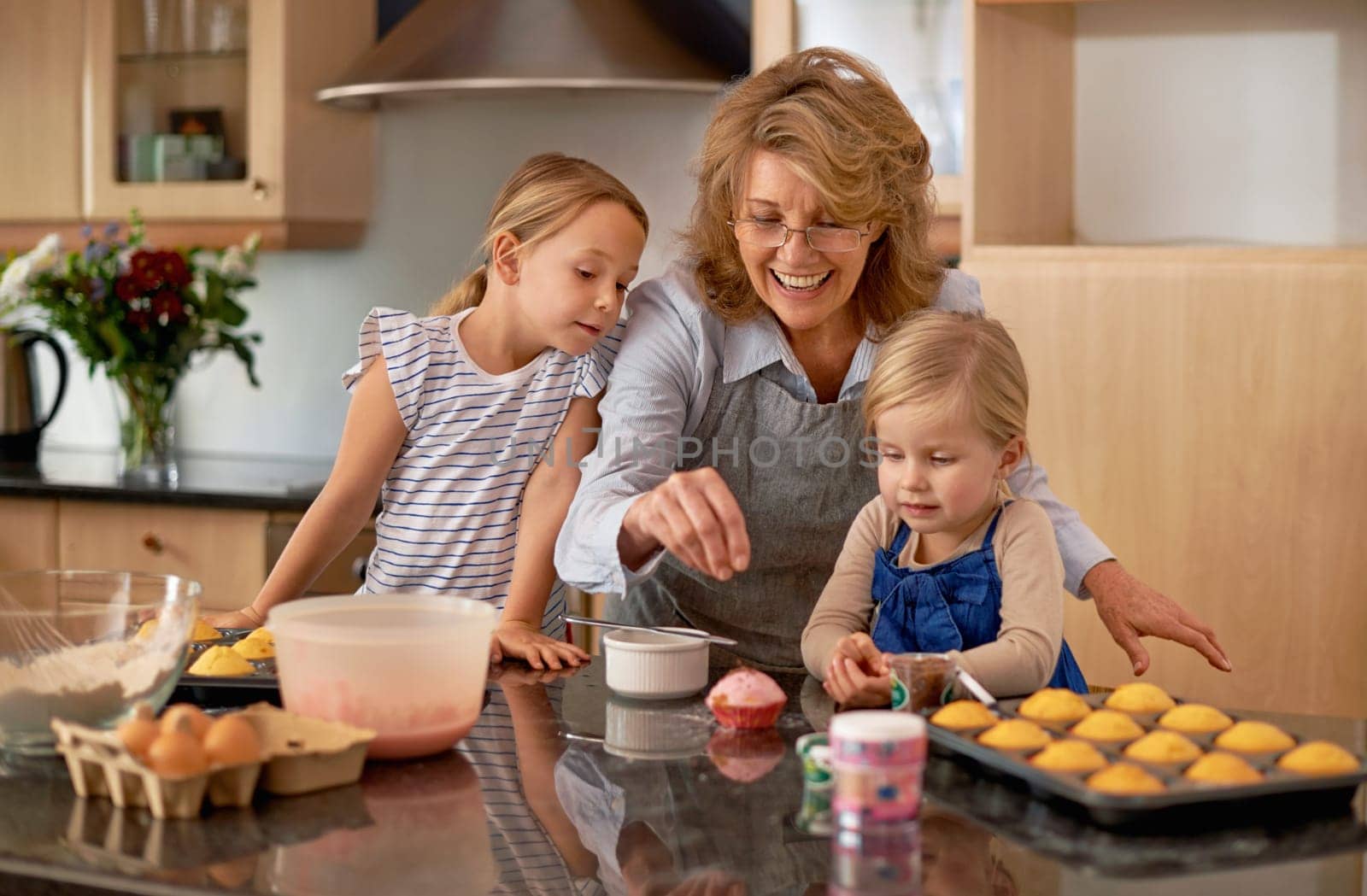 Grandma, kid and baking with teaching, smile and decorating for cheerful bonding together at home. Happy, pensioner or girl child with cupcake, laugh or icing for creative, playful or fun in kitchen by YuriArcurs