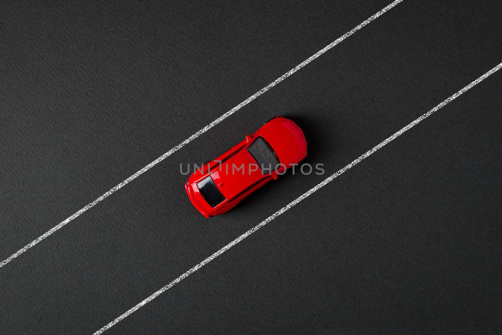 Top view of a red toy car driving on the drawn road line on a gray background by Sonat