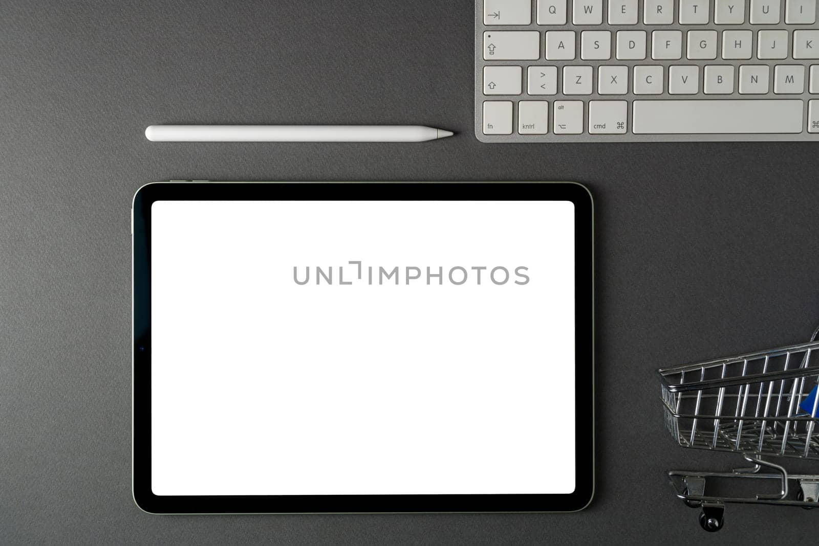 Tablet with blank screen, keyboard and supermarket cart on dark gray office desk