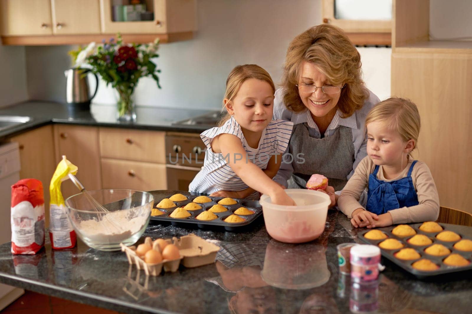 Grandmother, children and baking cupcakes or helping with icing decorations or learning creativity, bonding or teamwork. Woman, siblings and sweet treats or teaching with ingredients, snack or fun.