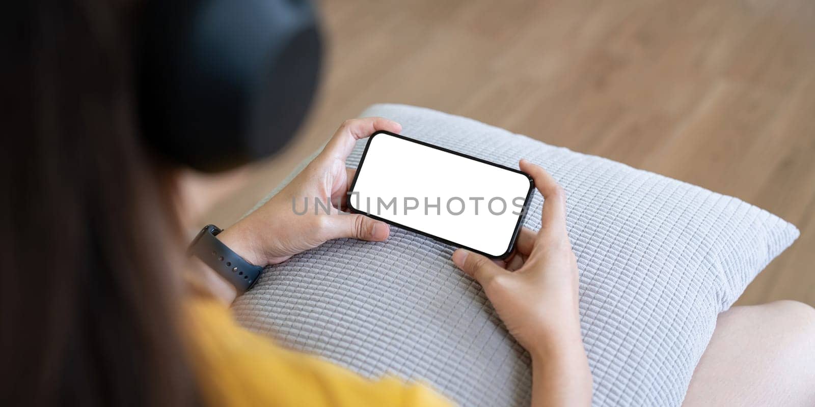 Mockup smartphone of a woman holding mobile phone with blank white screen while sitting listen to music at home.