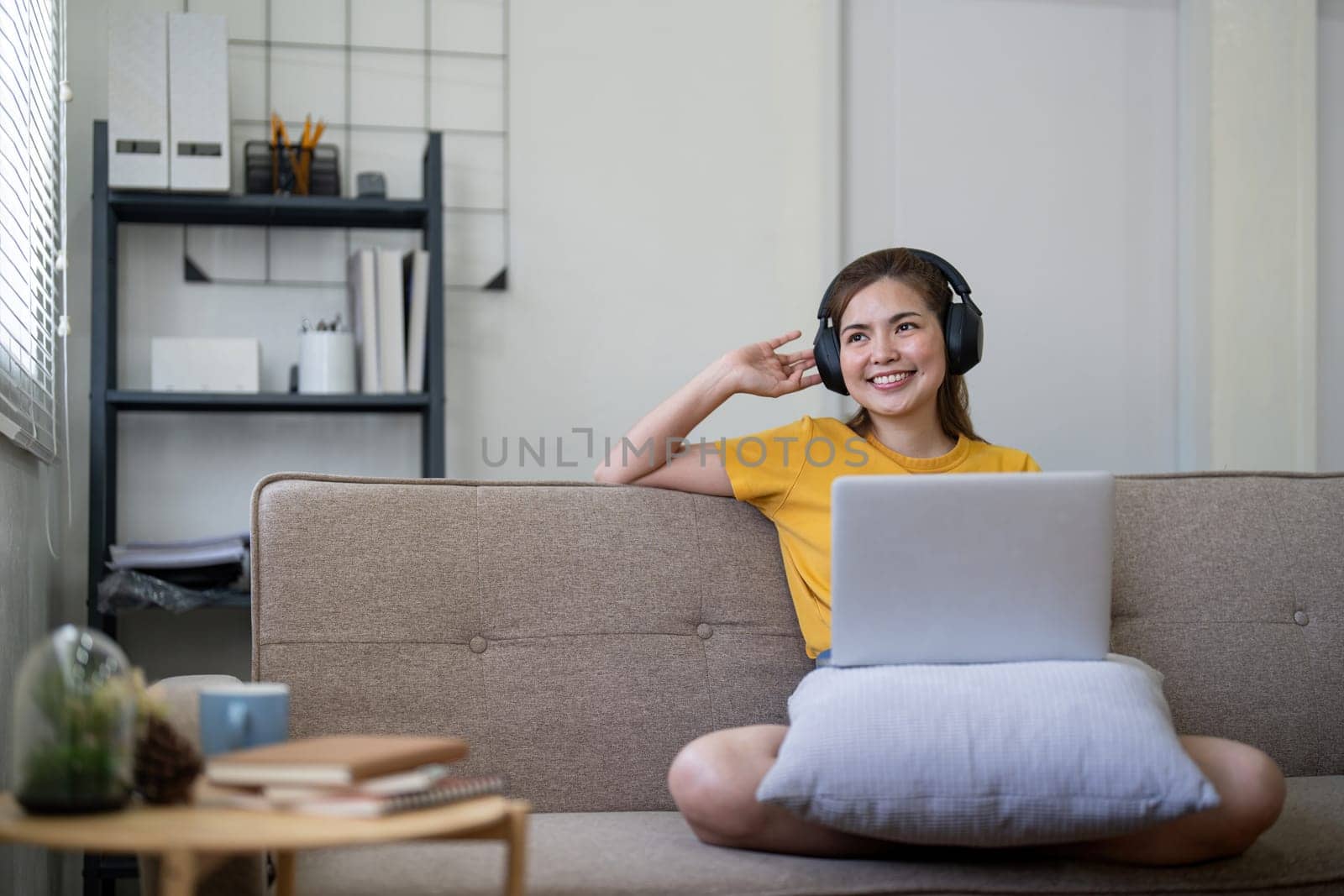 Young asian woman using laptop and earphones to listening to music at home.