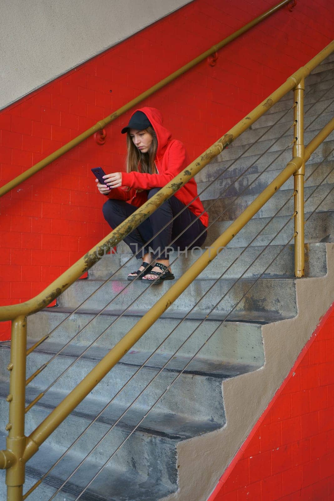 Young woman checking email on smartphone resting on stairs outdoors. Online message on cellphone Red colors. High quality photo