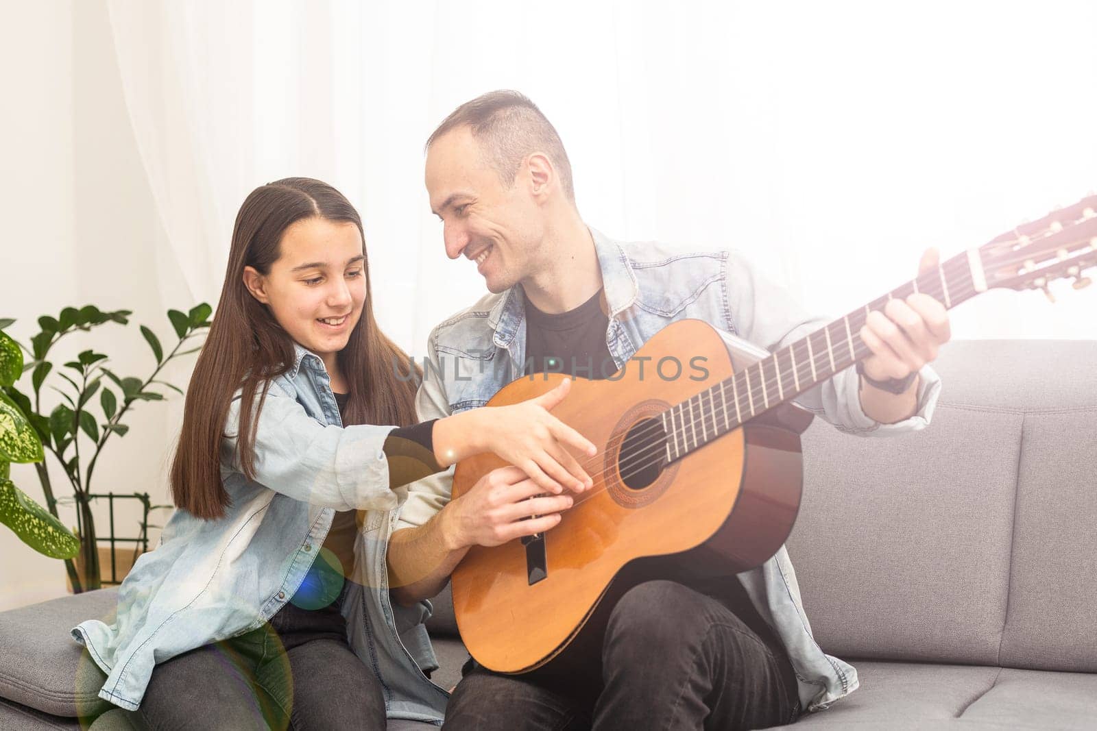 Father guy teaching girl teenager daughter guitar playing at home. Family musical lessons with strings instrument by Andelov13