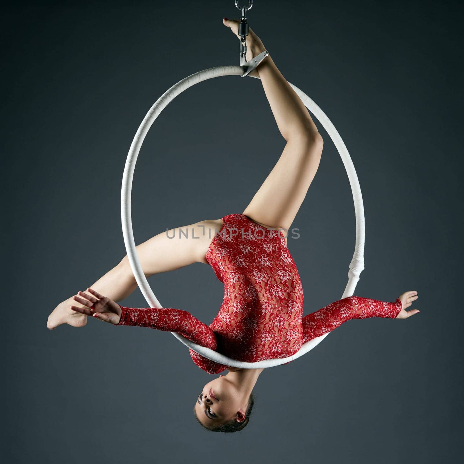 Studio photo of lovely gymnast performs acrobatic stunt on hoop
