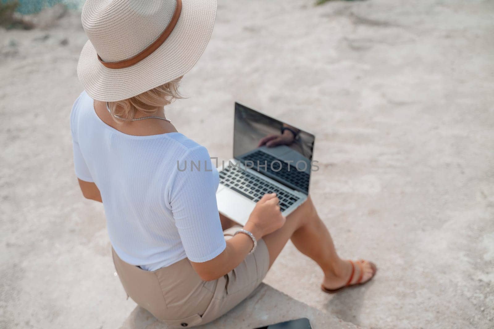 Freelance women sea working on the computer. Good looking middle aged woman typing on a laptop keyboard outdoors with a beautiful sea view. The concept of remote work. by Matiunina