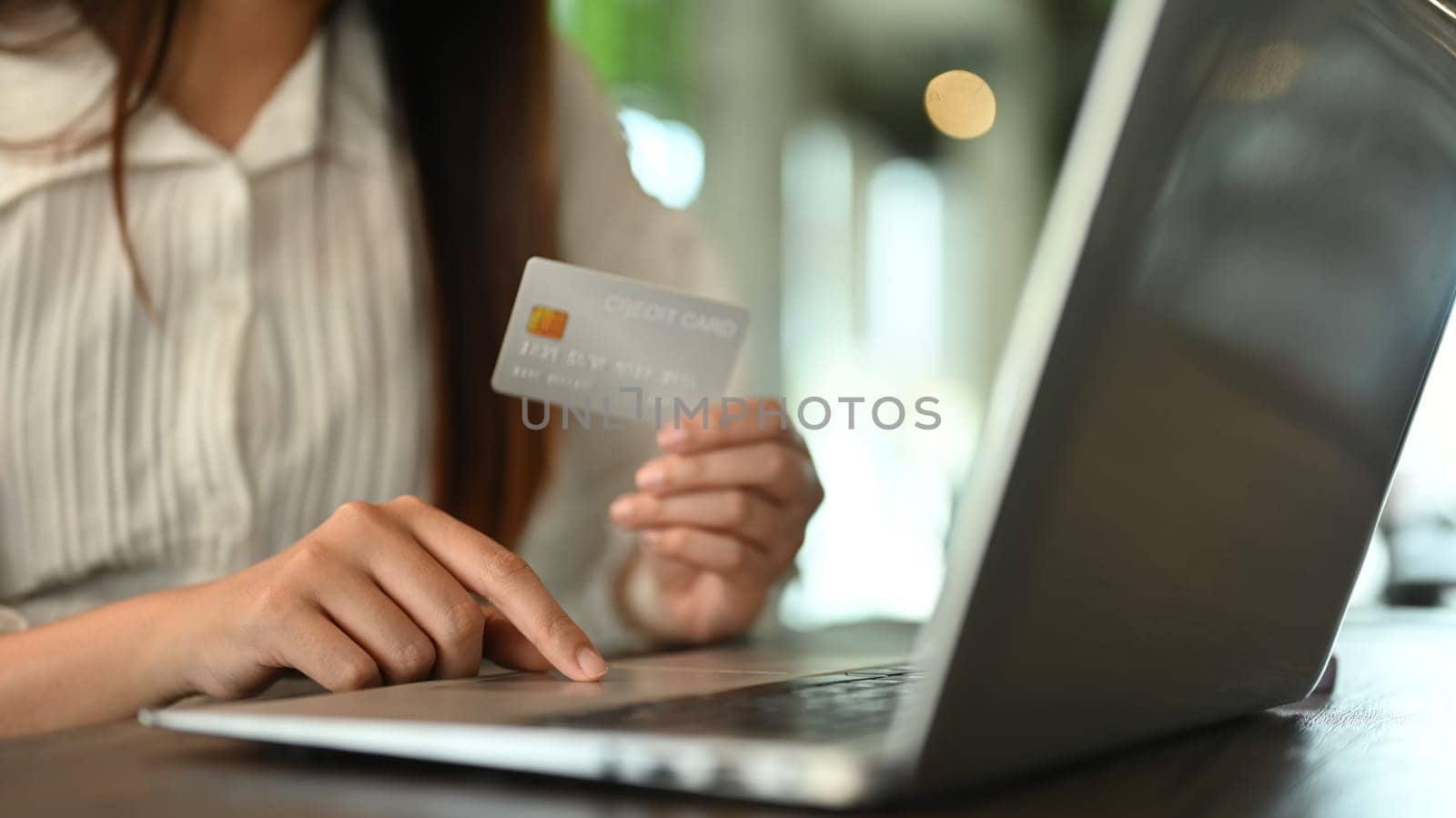 Closeup woman hand holding credit card and typing on laptop, making online shopping or paying bills.