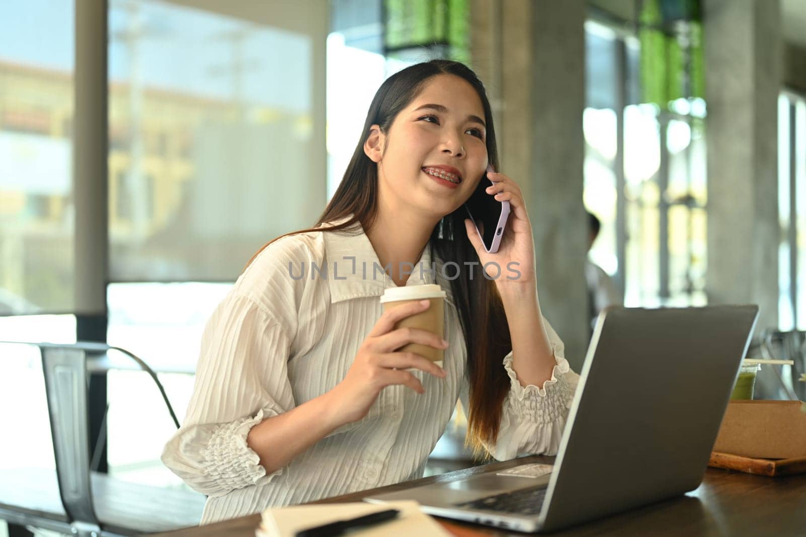 Charming young female entrepreneur drinking coffee and talking on mobile phone.