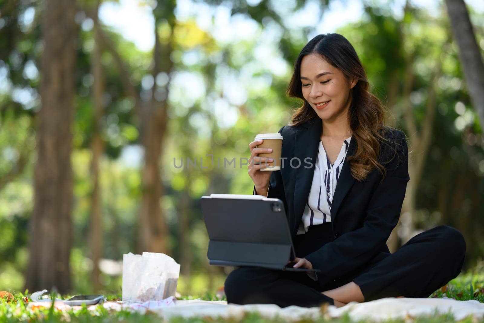 Millennial businesswoman working remotely outside office drinking coffee and using digital tablet.