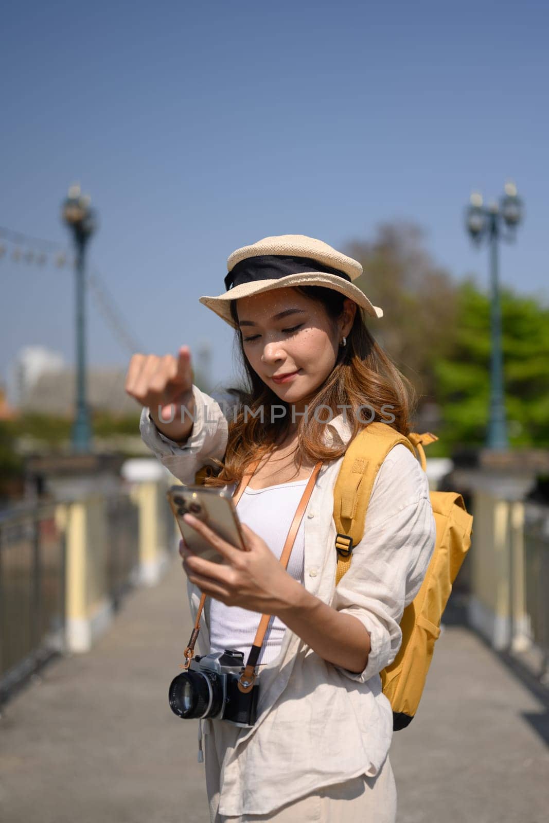 Female tourist searching direction on smart phone while sitting on bridge over river by prathanchorruangsak