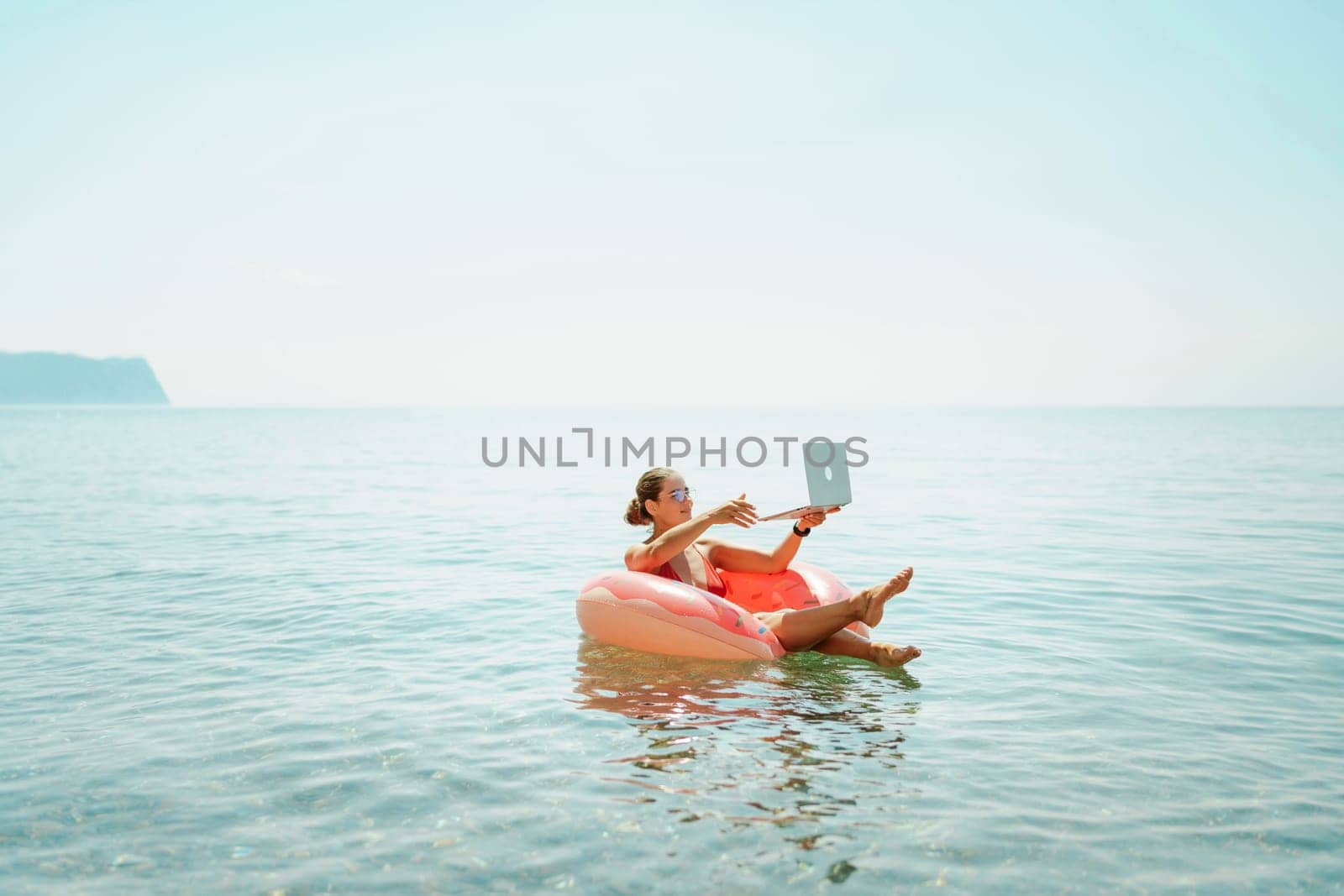 Woman laptop sea. Freelancer woman in sunglases floating on an inflatable big pink donut with a laptop in the sea. People summer vacation rest lifestyle concept by Matiunina