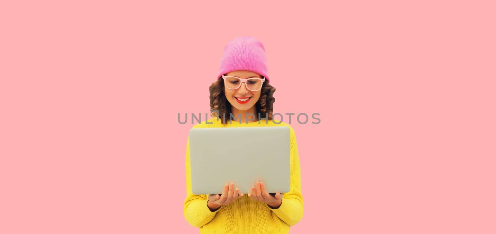 Stylish modern happy young woman working with laptop in colorful clothes on pink studio background by Rohappy