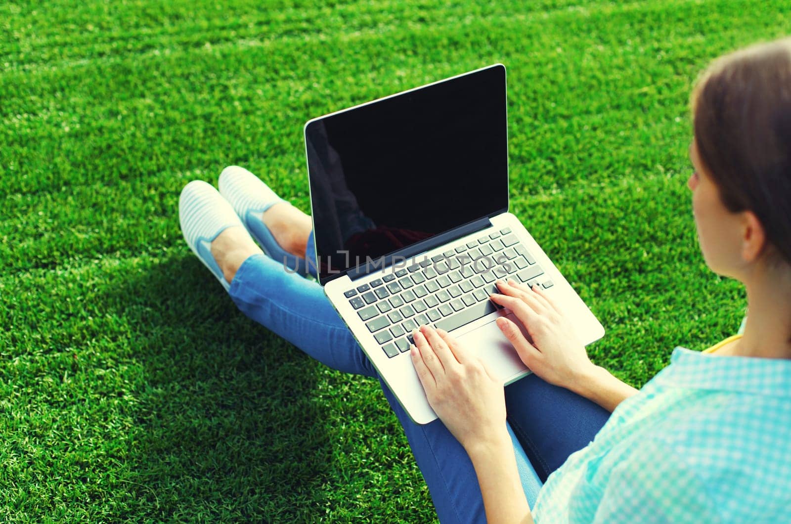 Female hands woman working with laptop, blank black screen in summer park on green grass background