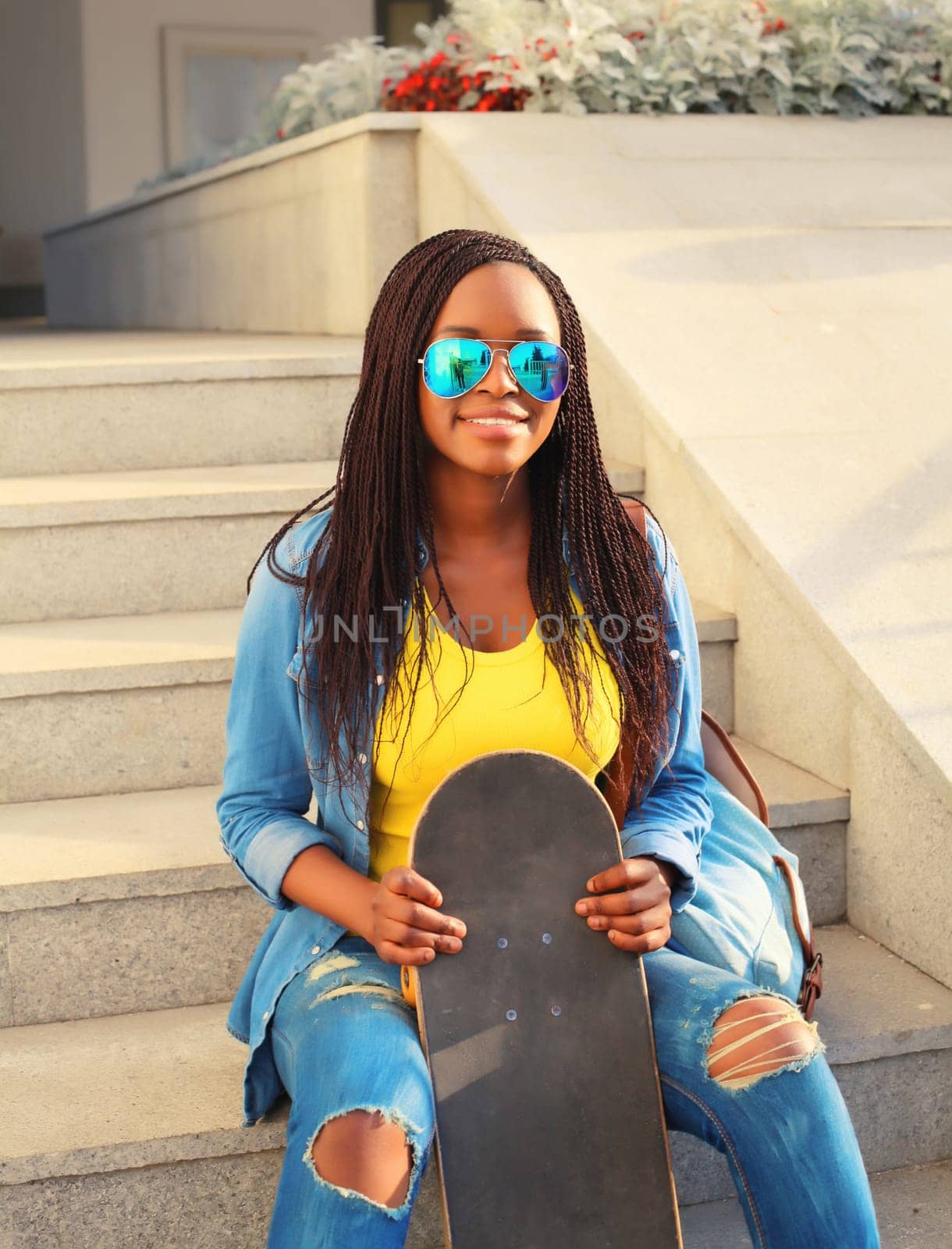 Portrait of happy smiling young african woman with skateboard in the city by Rohappy