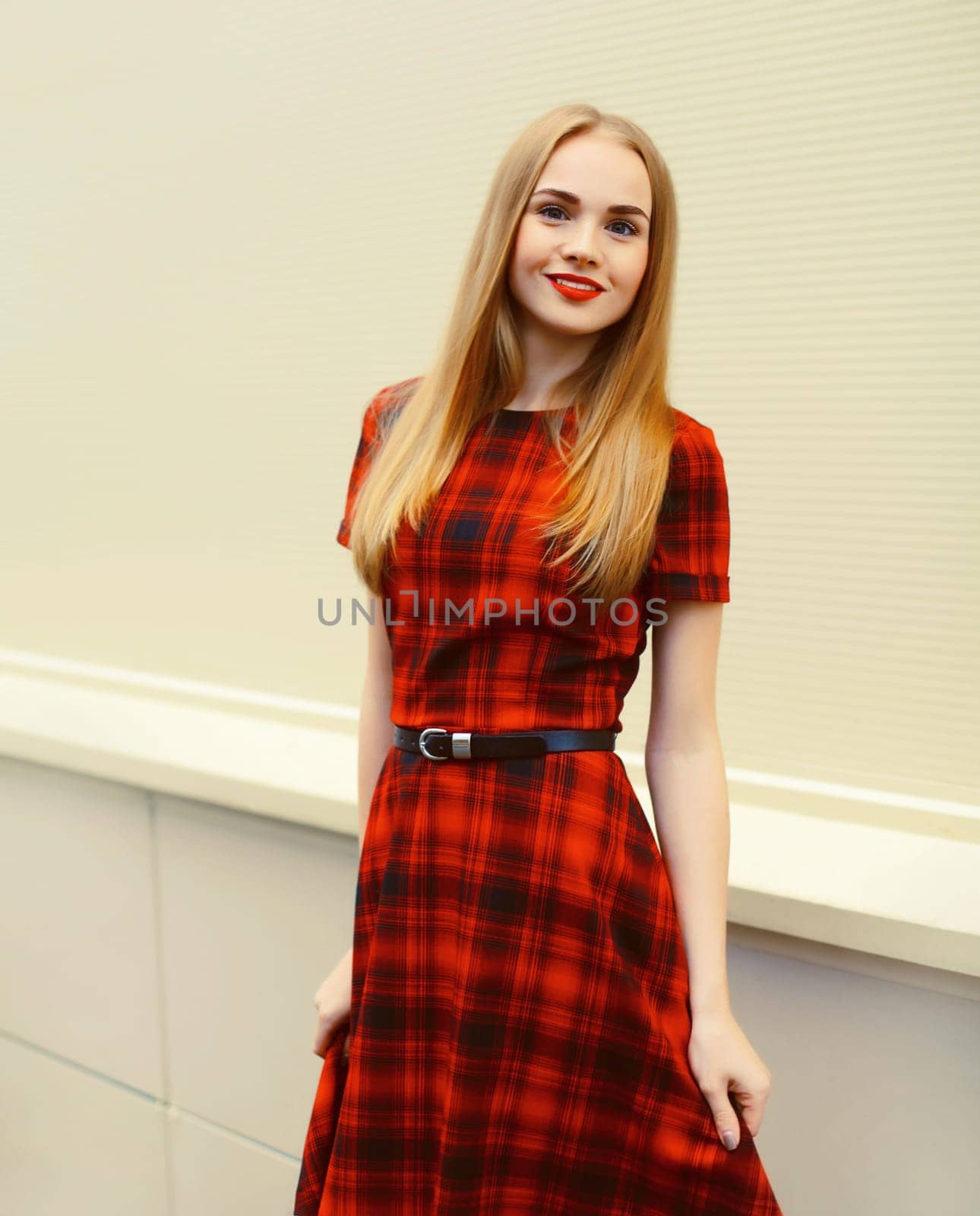 Portrait of beautiful smiling blonde young woman wearing red dress with scottish cell in the city