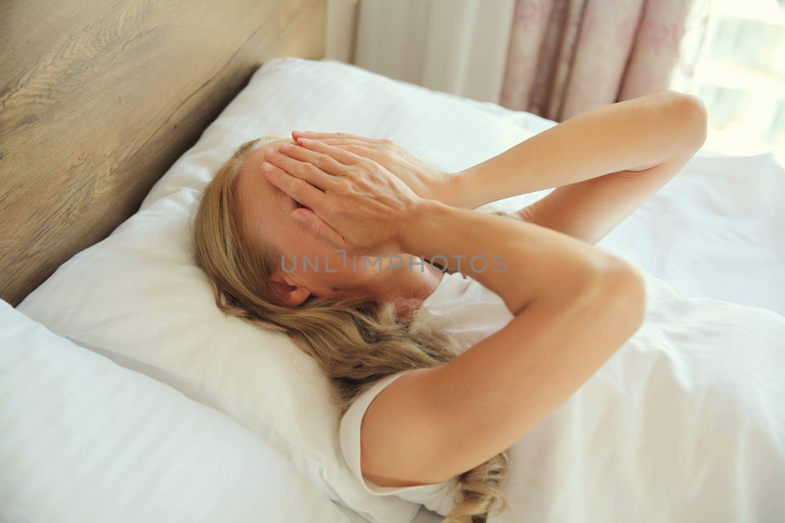Upset sad crying woman covering her eyes with her hands lying on the bed on pillow while experiencing mental suffering in bedroom at home