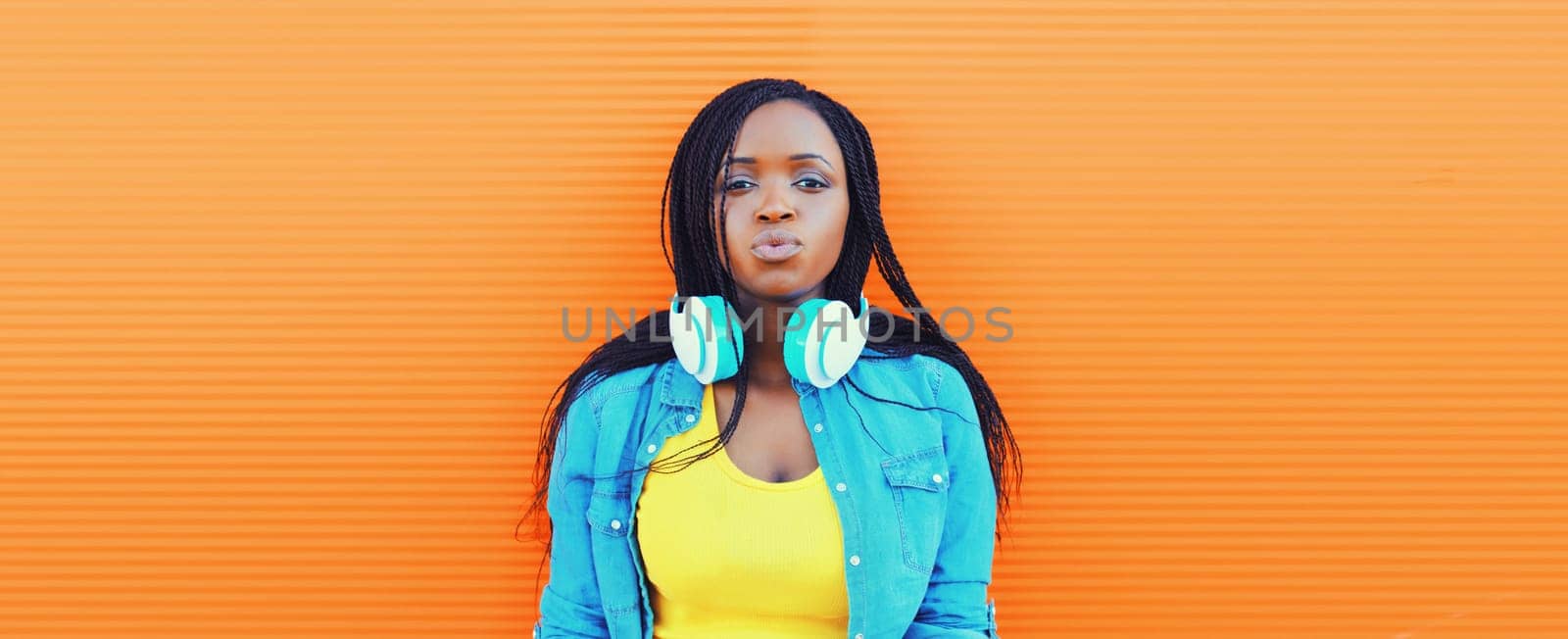 Portrait of young african woman listening to music in headphones on orange background