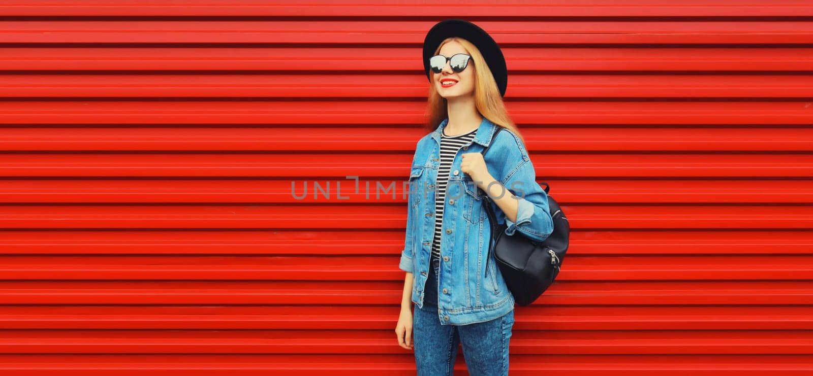 happy young woman looking away in black round hat, jean jacket, backpack on red background by Rohappy