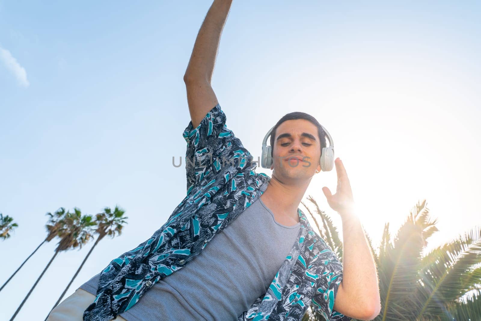 Trendy young male in headphones dancing enjoying music outdoor on summer resort. by PaulCarr