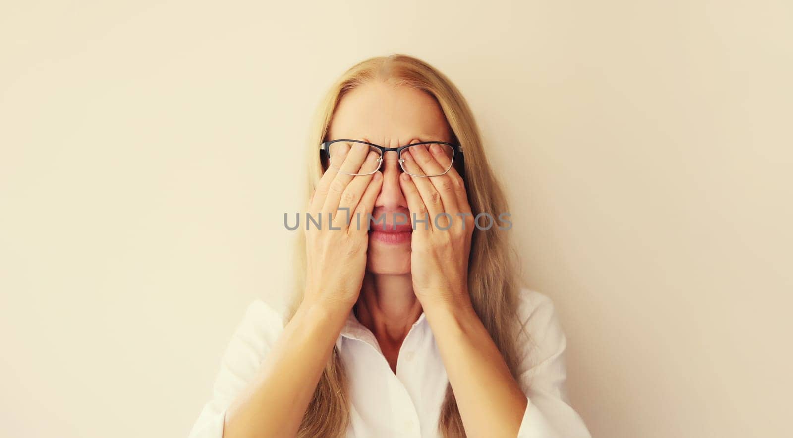 Tired overworked middle-aged woman employee rubbing her eyes suffering from eye strain, dry eye syndrome or headaches after working at the computer