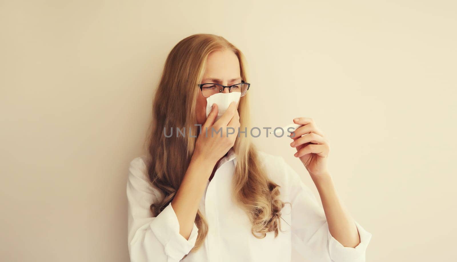 Sick exhausted caucasian woman employee sneezing blow nose using tissue and measuring checking body temperature looking at thermometer at home