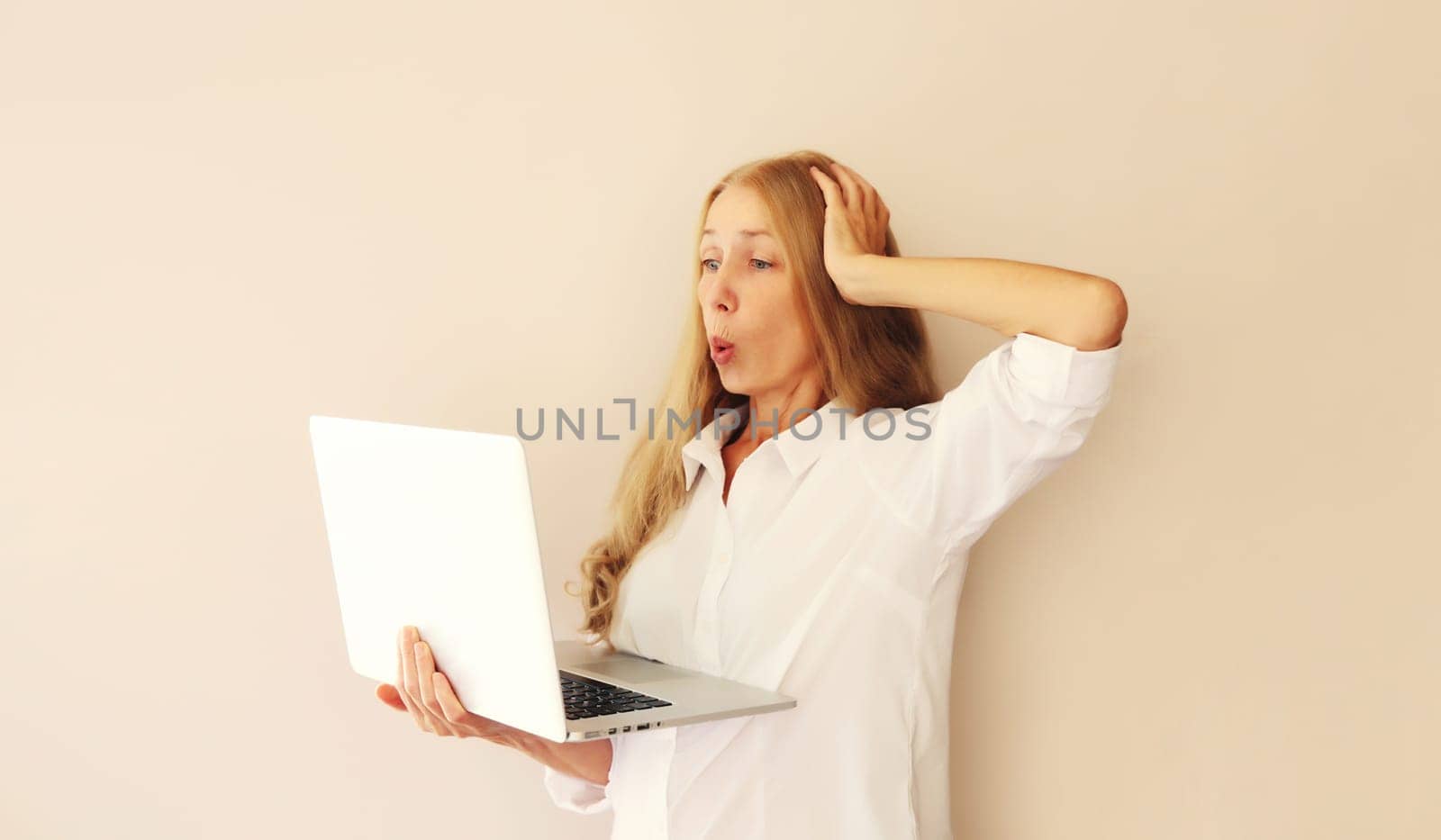 Surprised middle-aged woman looking at laptop at home by Rohappy