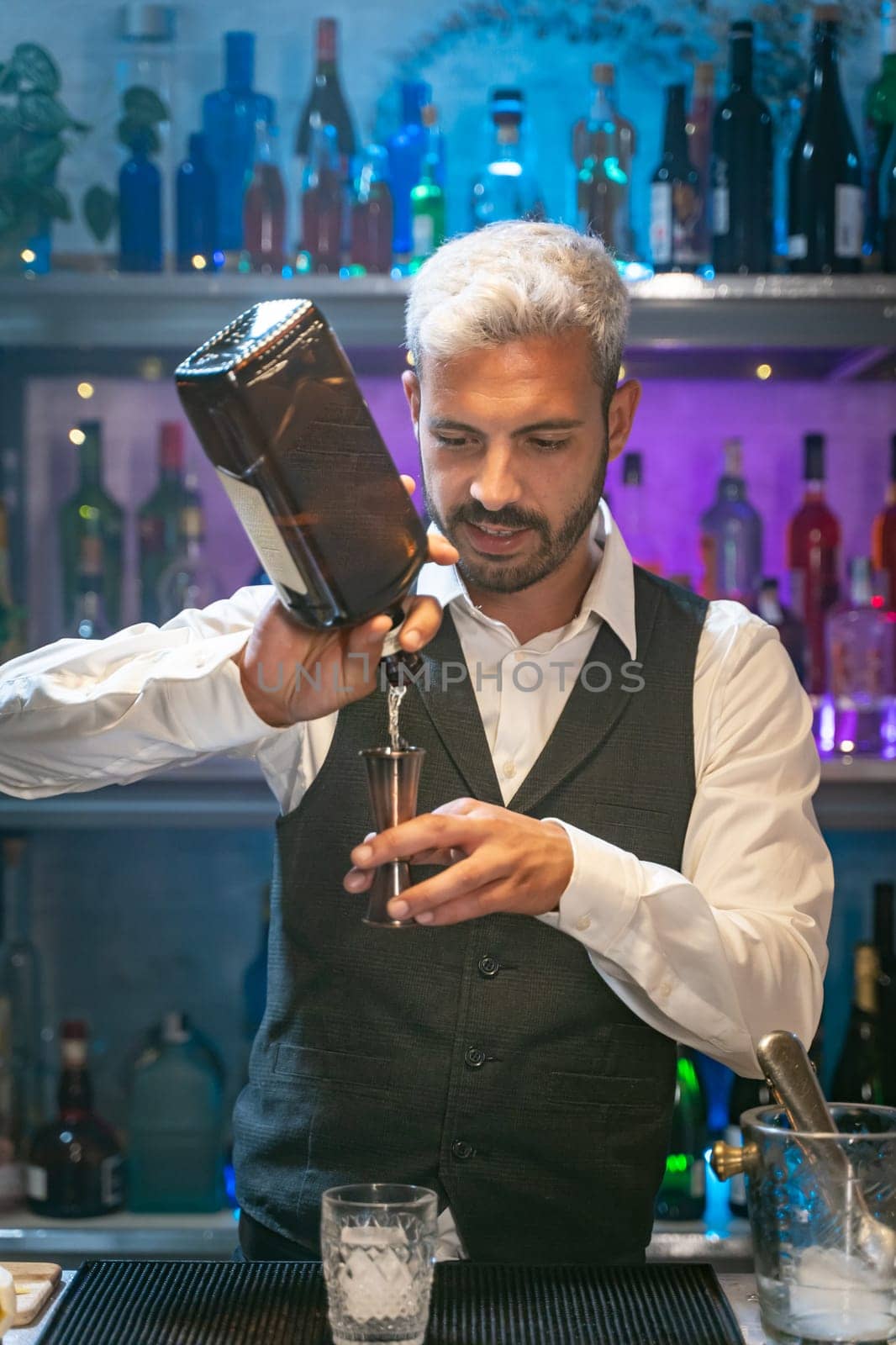 Professional barman in a white shirt and black apron making cocktail at party in nightclub. Nigh life. High quality photo