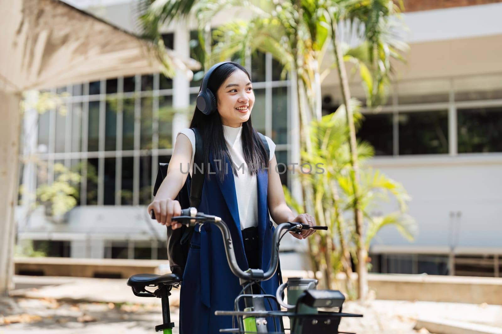 Asian young businesswoman bike to work for eco friendly green energy and listen music with headphone while commuting in city. Eco friendly by itchaznong