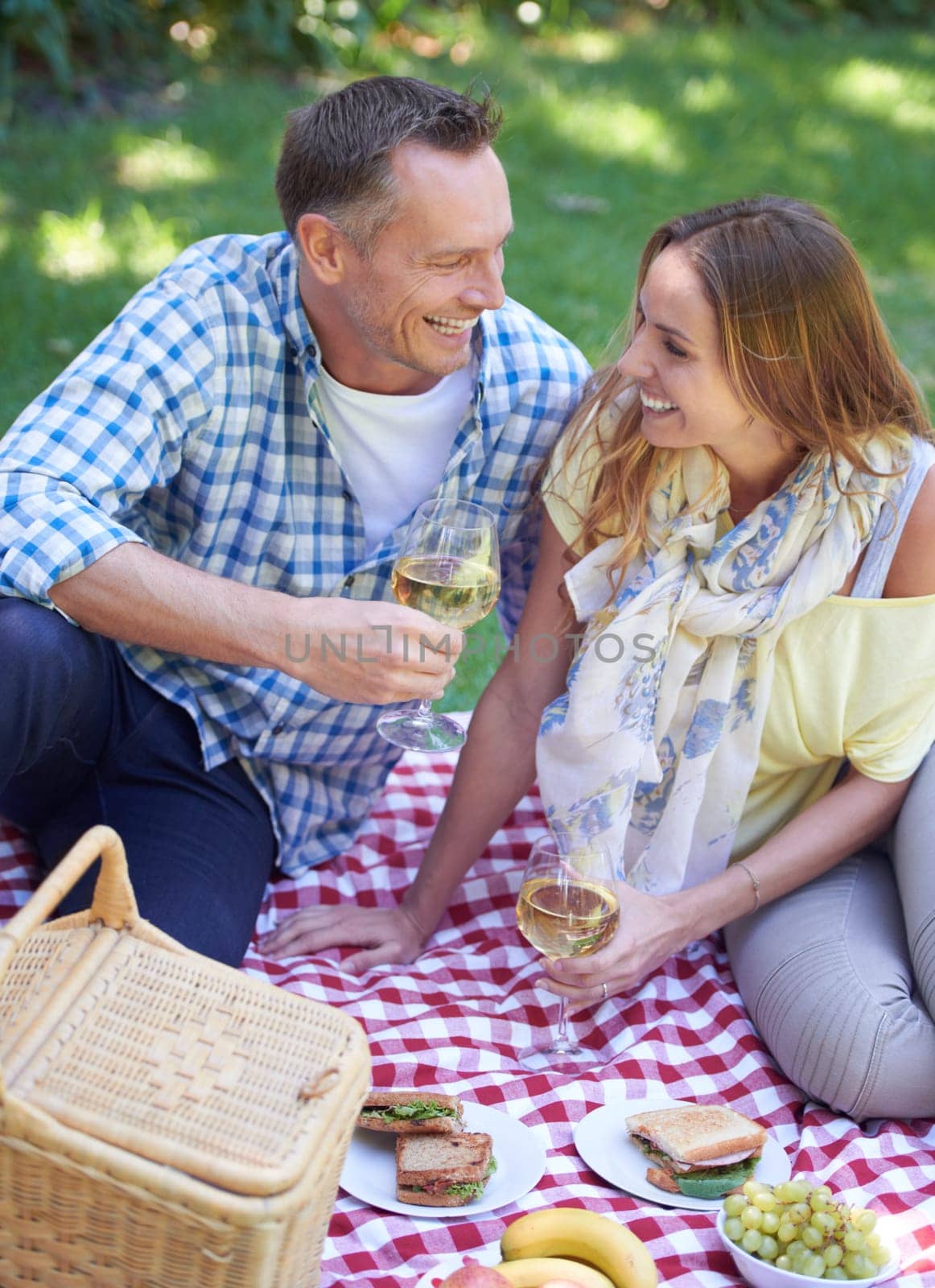 Couple, picnic and alcohol for bonding in outdoor nature, love and romance in relationship on weekend. Wine glasses, conversation and people on date in countryside, adventure and forest for happy by YuriArcurs