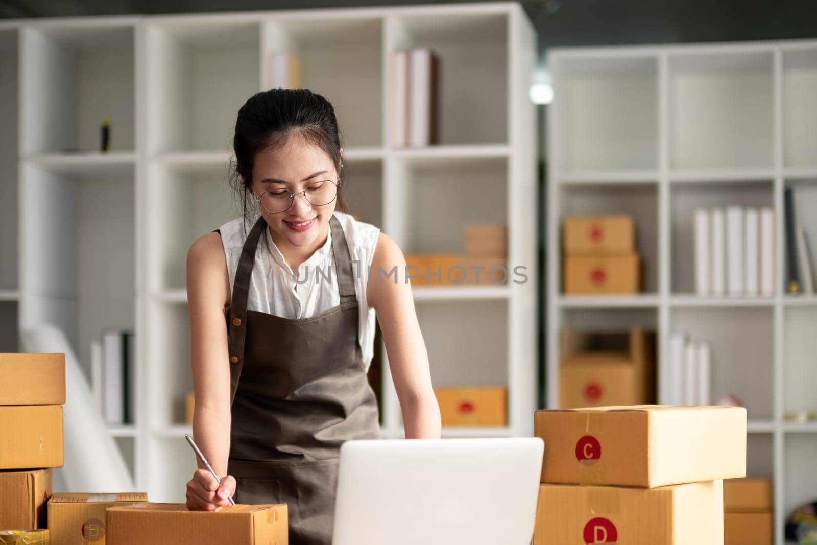 Young woman working online ecommerce shopping at her shop. Young woman sell prepare parcel box of product for deliver to customer. Online selling, ecommerce. Selling products online by nateemee