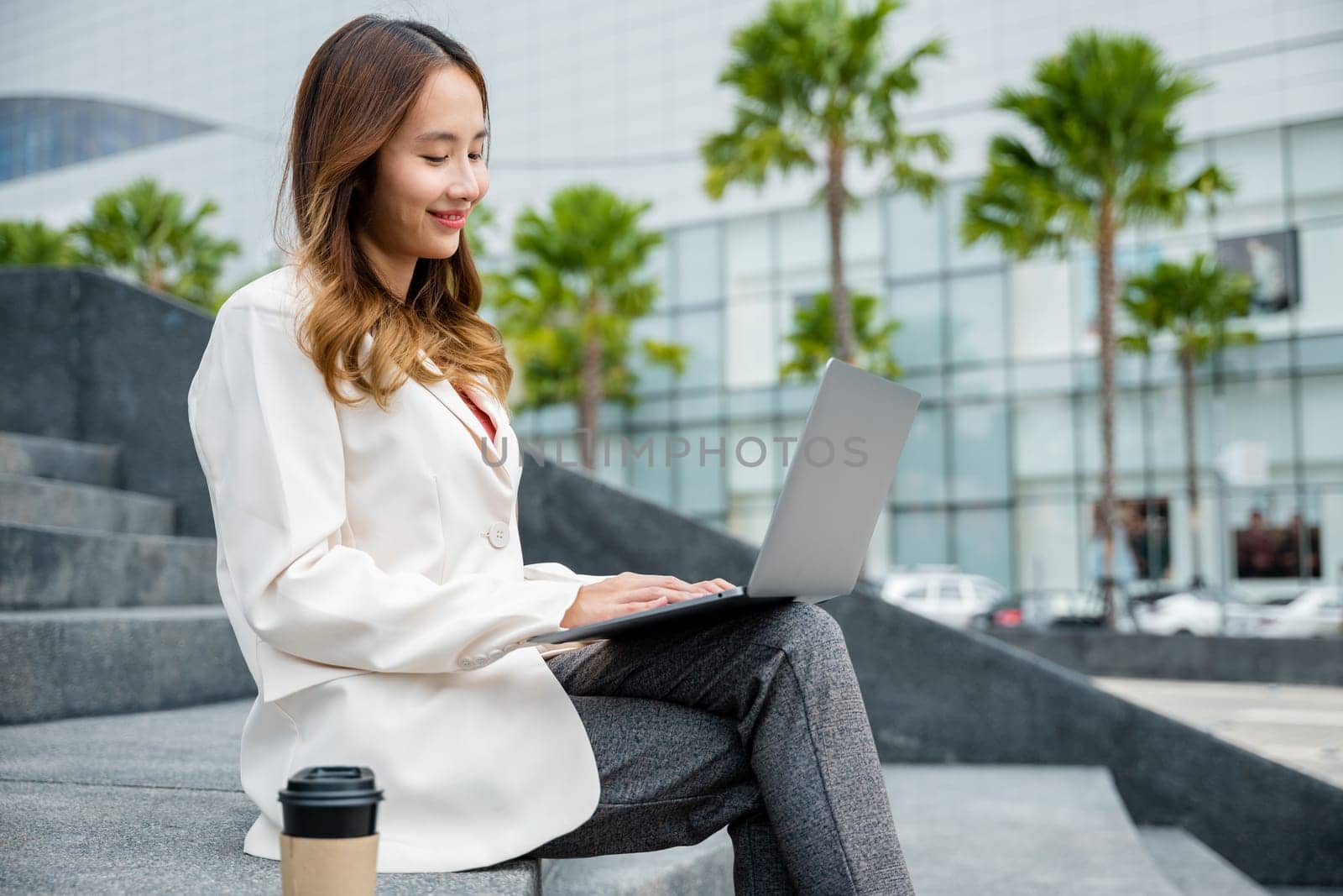 woman freelance looking laptop with smile while working with coffee cup while sitting on stairs by Sorapop