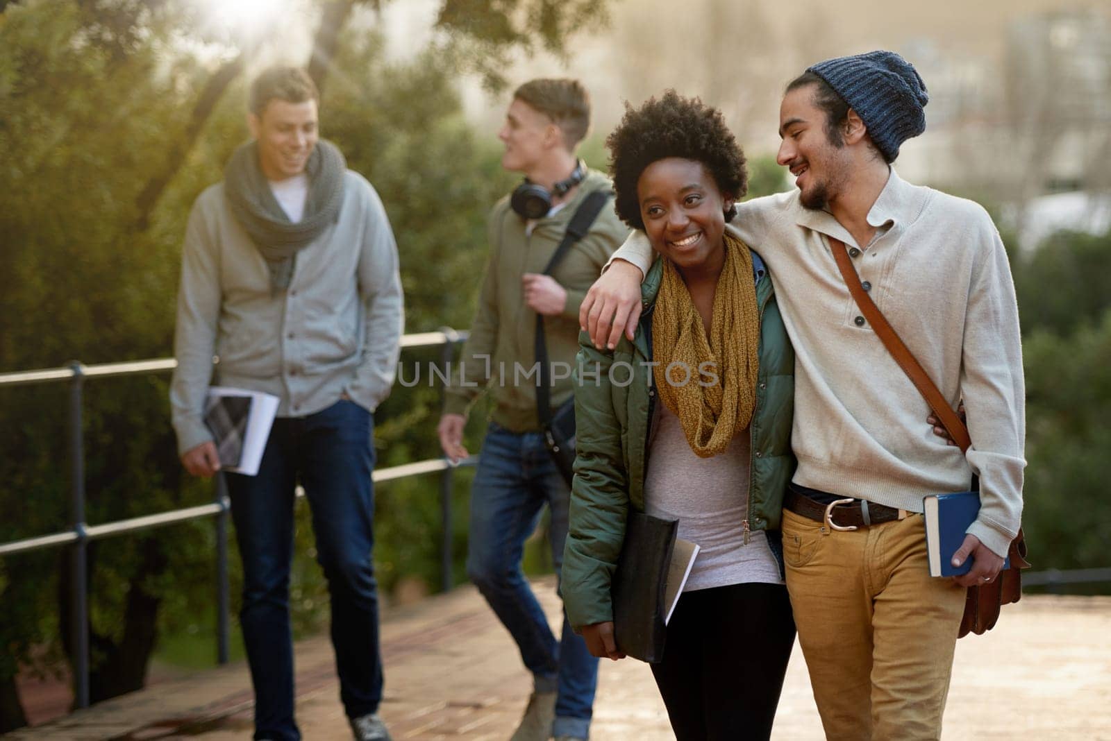 Interracial, couple and college student with hug in outdoor, campus and happy with love, support and care. University, education and texbook with notes for research to study for exams and assessment by YuriArcurs