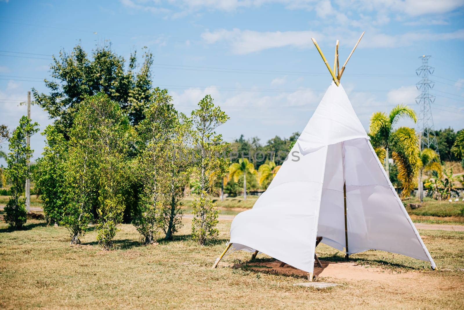 A charming summer wedding teepee stands in a green field evoking joy and celebration by Sorapop