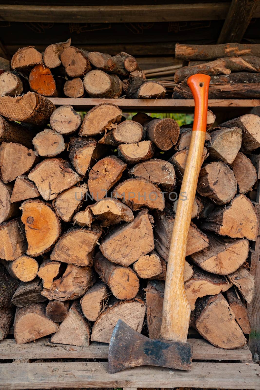 Axe in front of a stack of wood in a woodshed. Natural vertical background. High quality photo