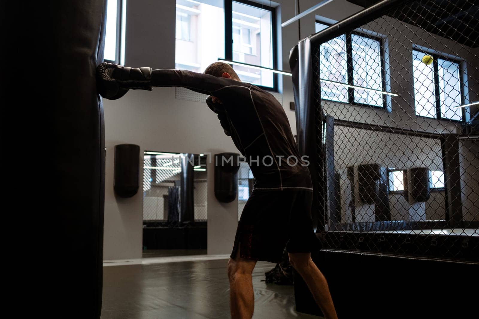 Determined adult man in sportswear and boxing gloves training with heavy bag in gym. Concept of cardiovascular high-intensity, full-body workout to burn calories, build muscle, and improve endurance