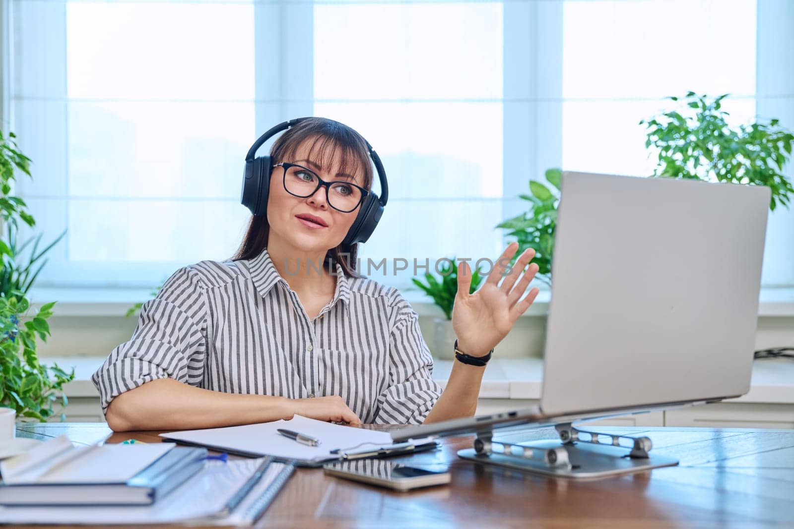 Middle-aged woman in headphones working at computer in home office by VH-studio