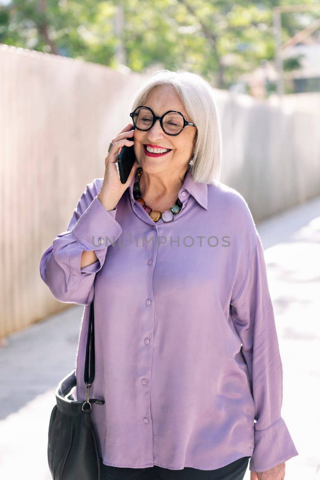 beautiful senior woman smiling happy while walking on the street talking on the phone, concept of technology and elderly people leisure