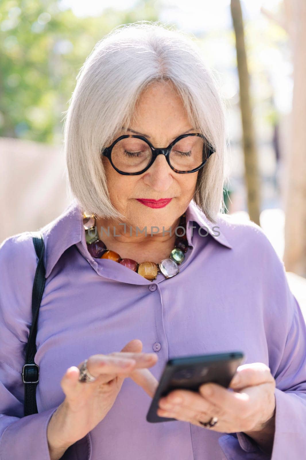 portrait of beautiful senior woman typing on mobile phone on the street, concept of technology and elderly people leisure