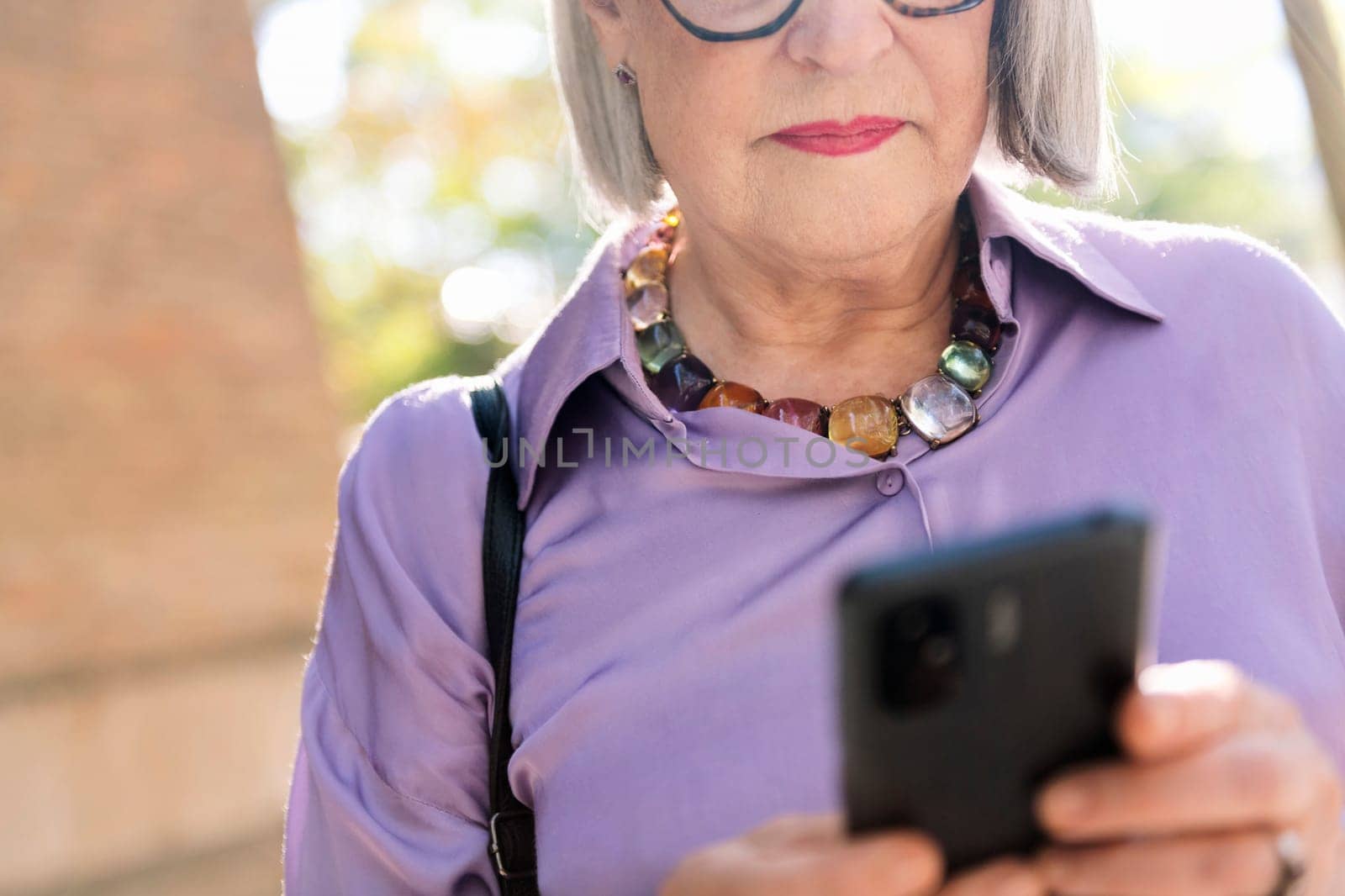 unrecognizable senior woman using mobile phone on the street, concept of technology and elderly people leisure