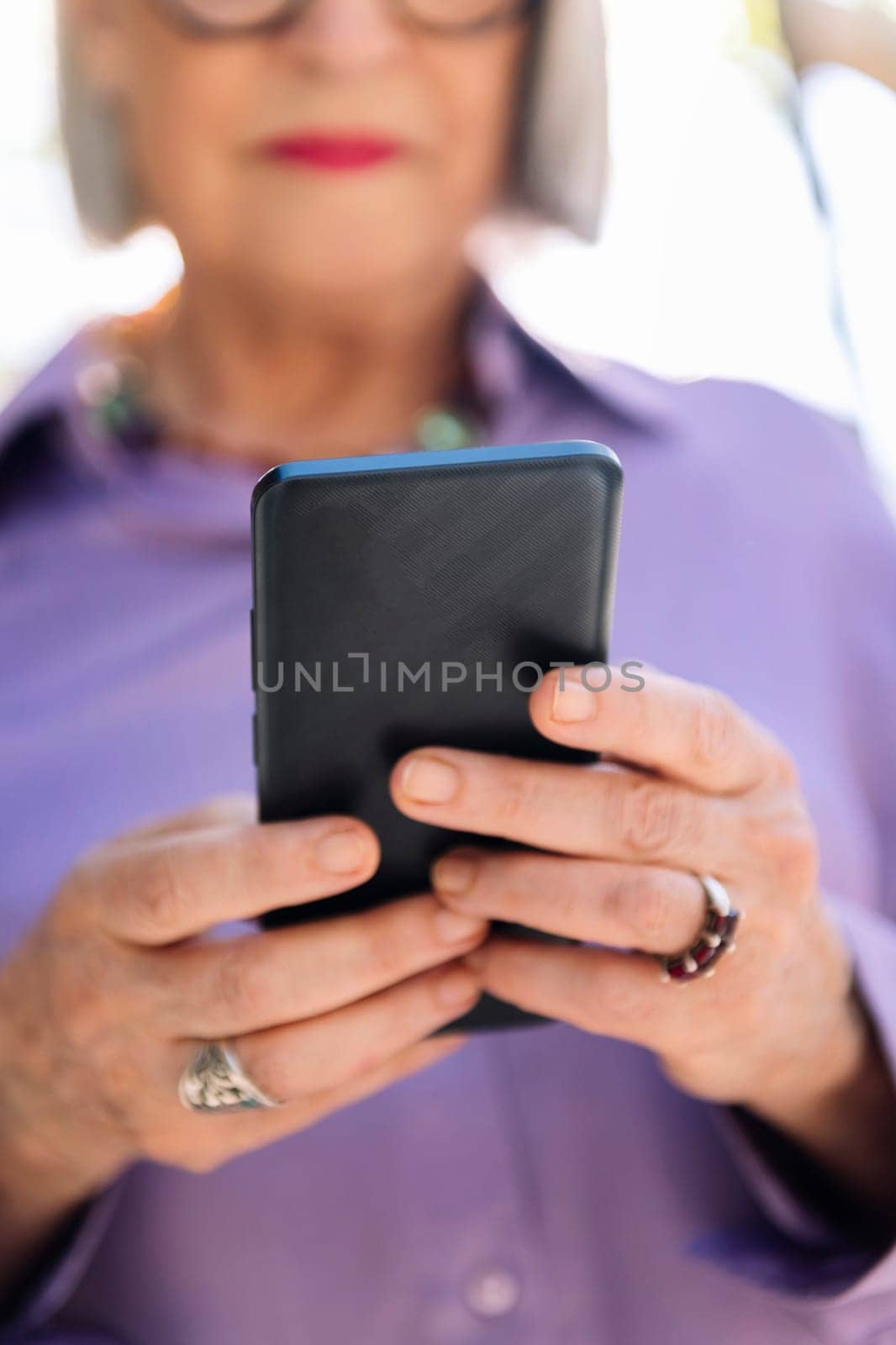 unrecognizable senior woman using mobile phone on the street, focus on the phone, concept of technology and elderly people leisure