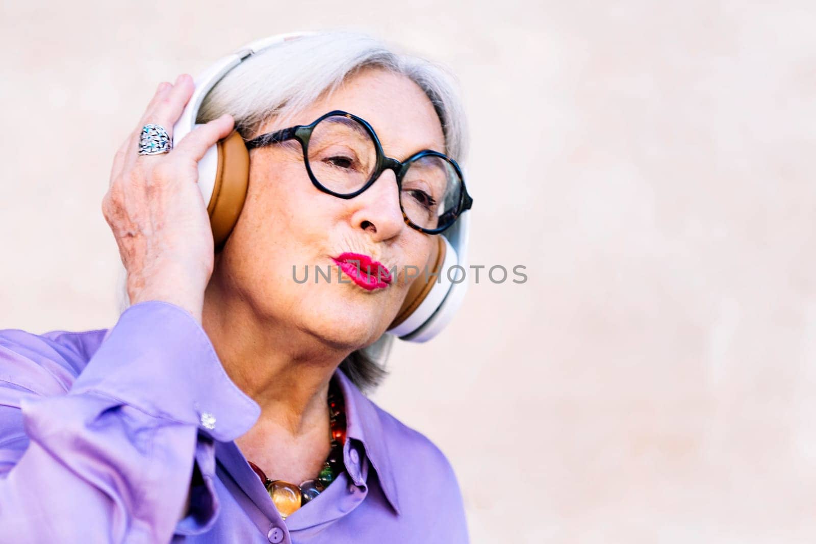 happy senior woman in glasses enjoying music in her headphones, concept of elderly people leisure and active lifestyle, copy space for text