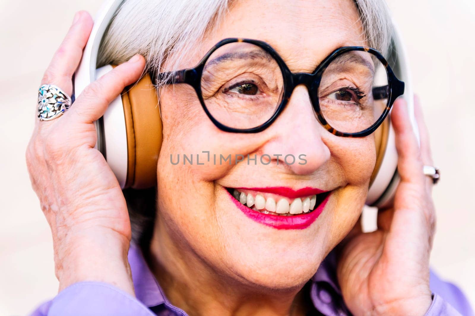 close up portrait of a smiling senior woman in glasses enjoying listening to music in her headphones, concept of elderly people leisure and active lifestyle