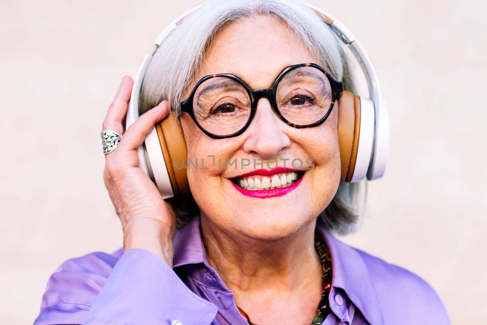 close up portrait of a smiling senior woman looking at camera enjoying listening to music in her headphones, concept of elderly people leisure and active lifestyle
