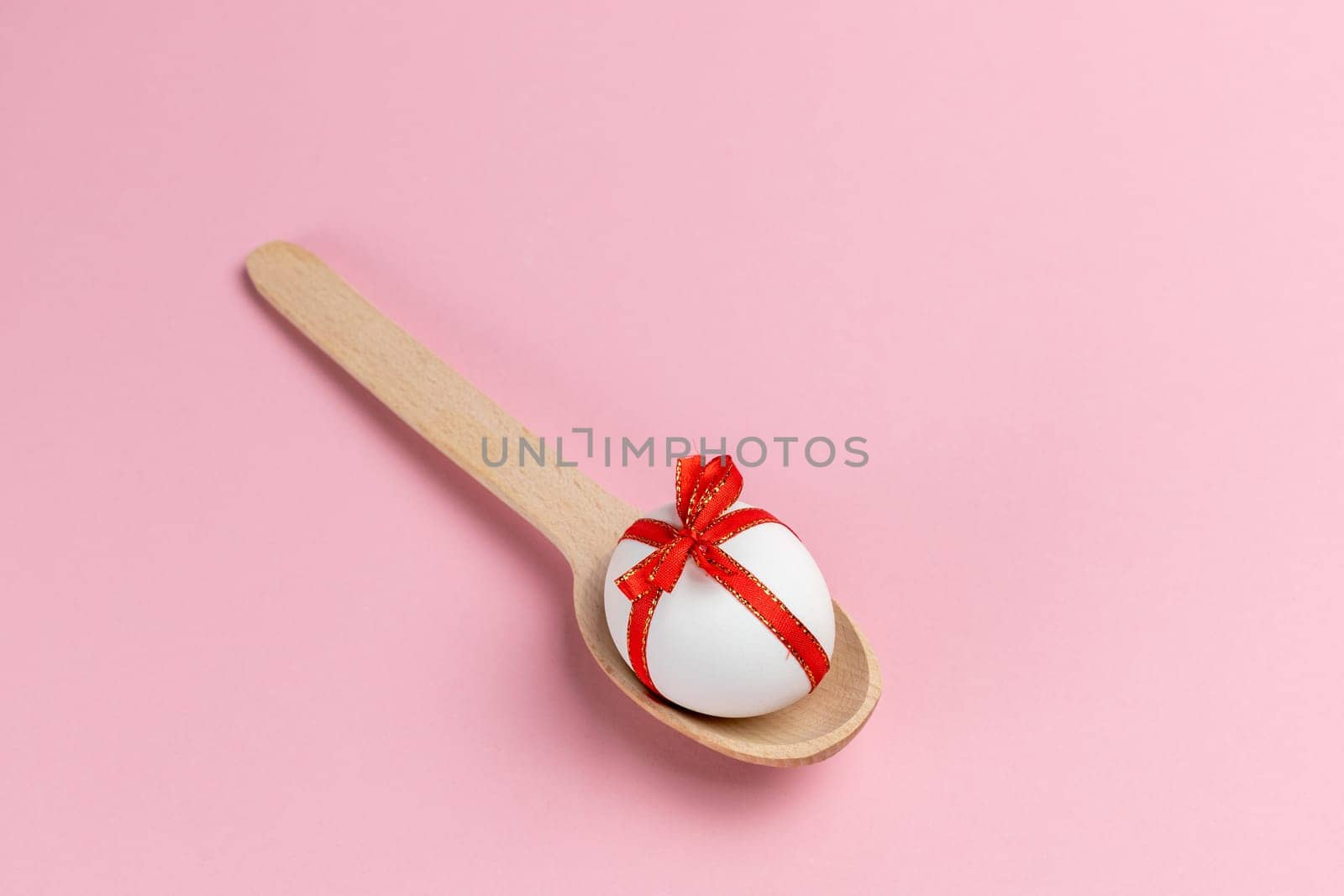 Easter egg with the wooden spoon on the pink background. Top view.